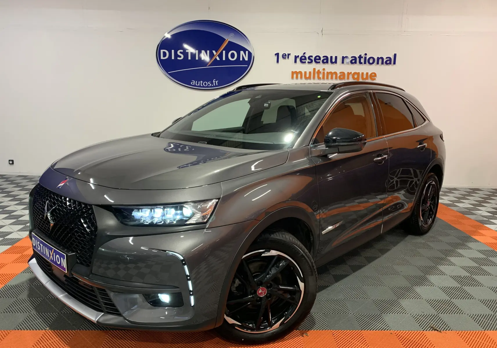 DS7 Crossback gris Platinium en 3/4 avant droit avec phares allumés et jantes noires brillantes.