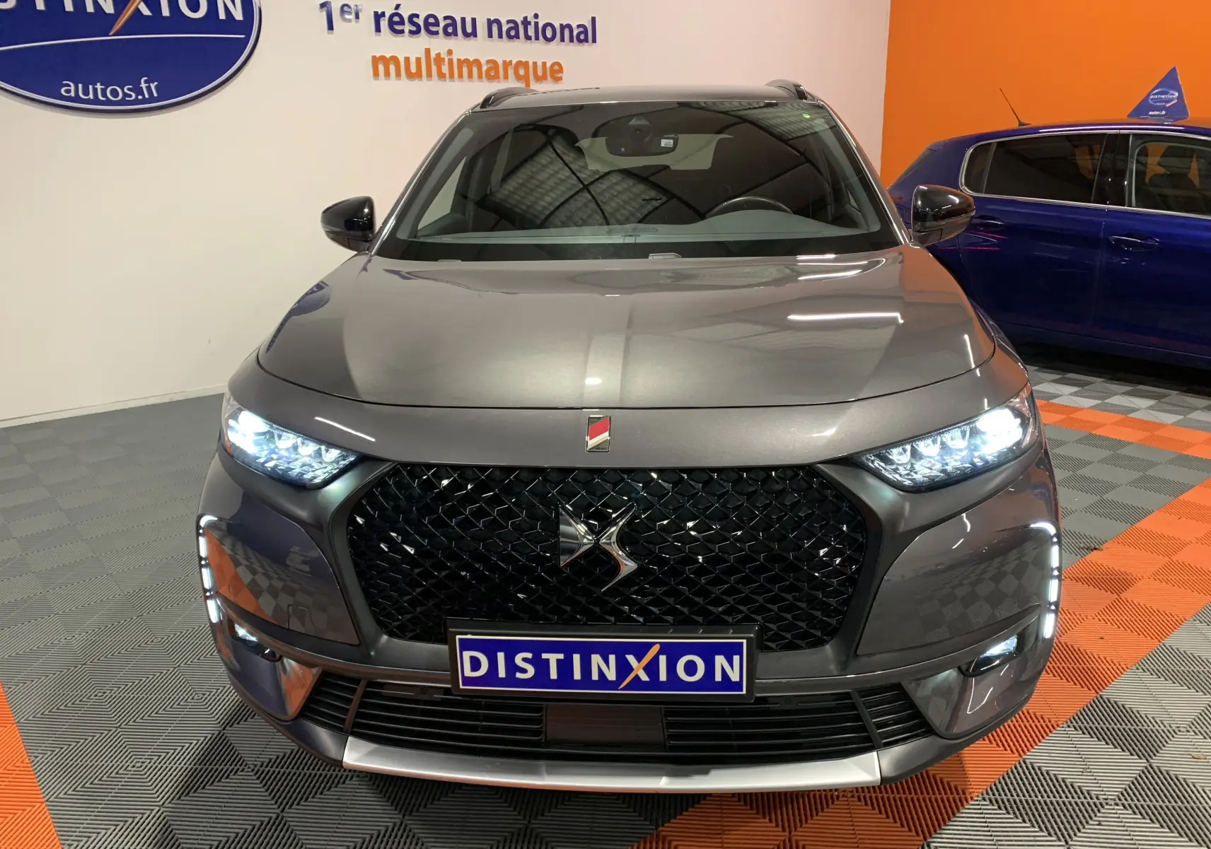Vue frontale d'un DS7 Crossback gris Platinium avec phares allumés et calandre noire distinctive.