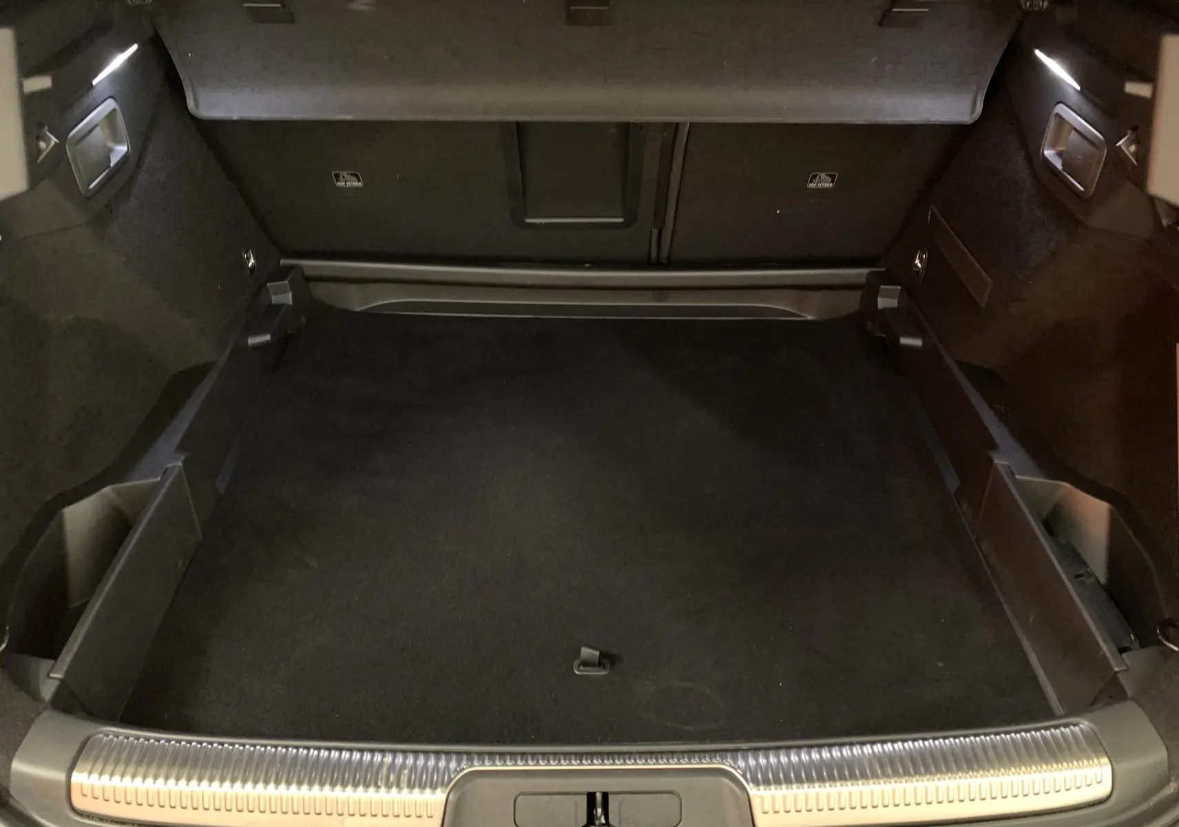 Coffre spacieux du DS7 Crossback gris Platinium vu de l'arrière, avec tapis noir et finitions métalliques sur le seuil.