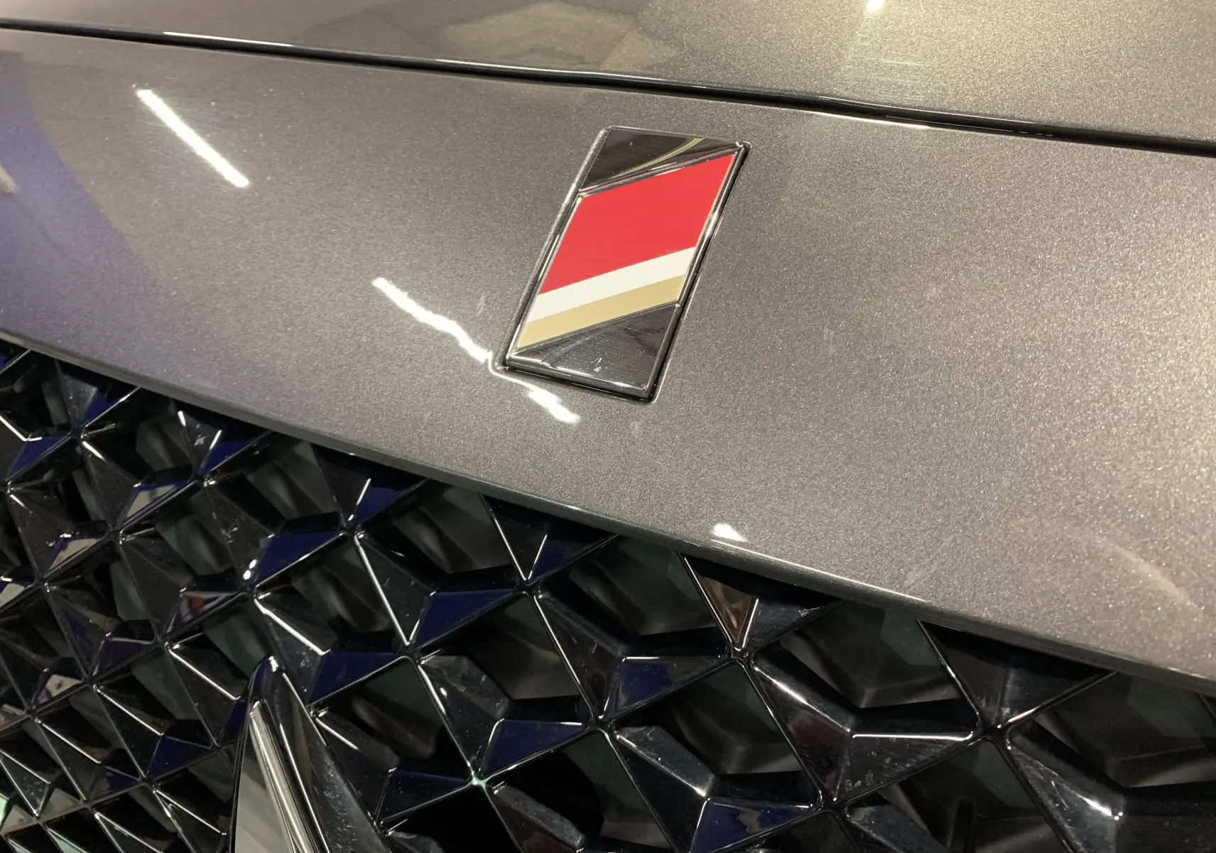 Gros plan sur la calandre noire et le logo tricolore du DS7 Crossback gris Platinium, vue avant centrée.