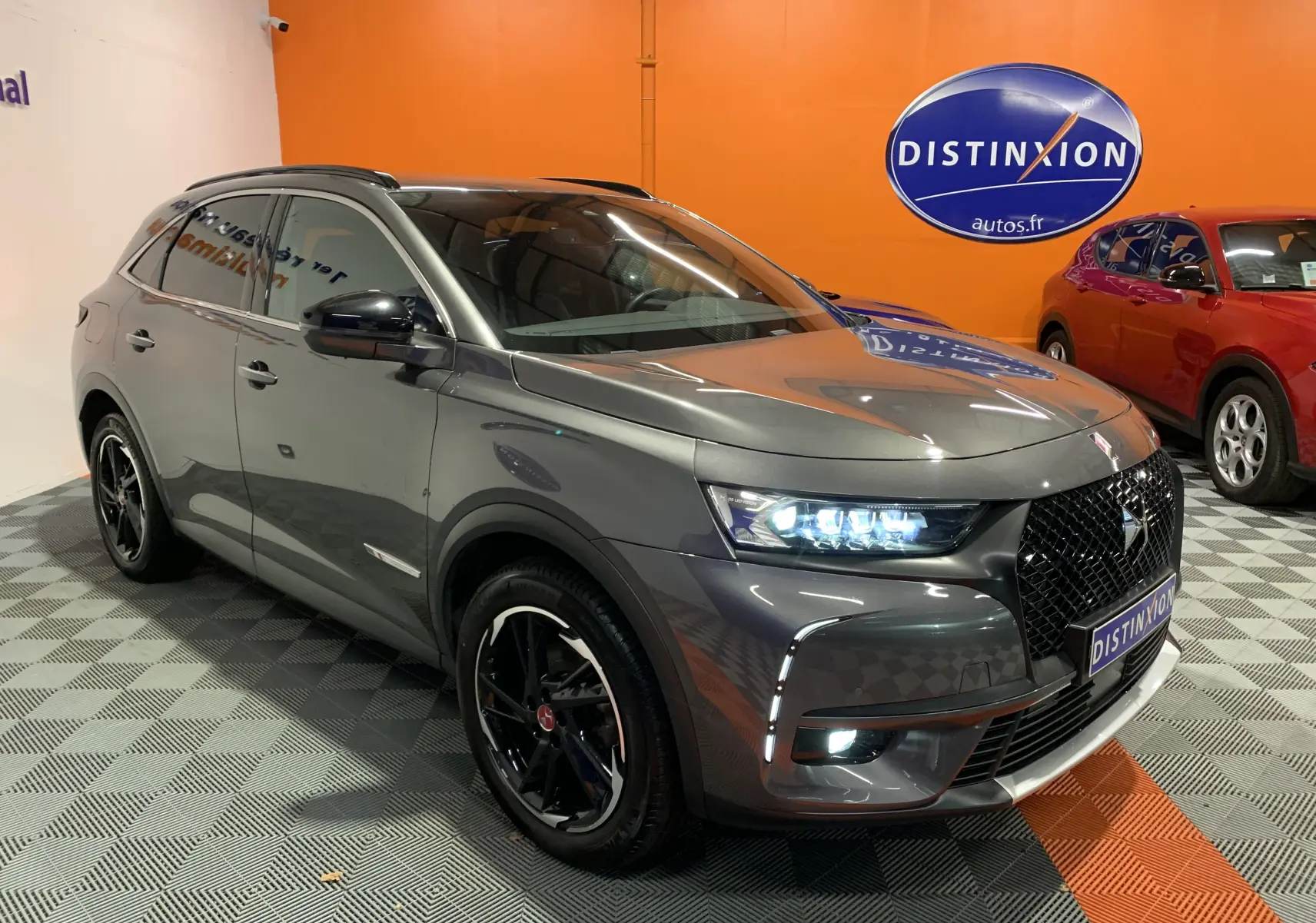 DS7 Crossback gris Platinium en 3/4 avant droit, phares LED allumés et jantes noires distinctives dans un showroom.