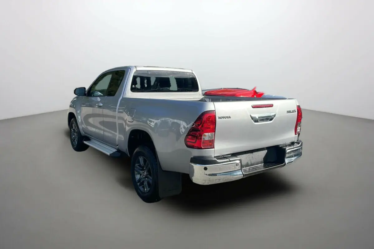 Toyota Hilux 4x4 gris acier vu en 3/4 arrière droit, avec benne chargée et détails chromés sur pare-chocs.
