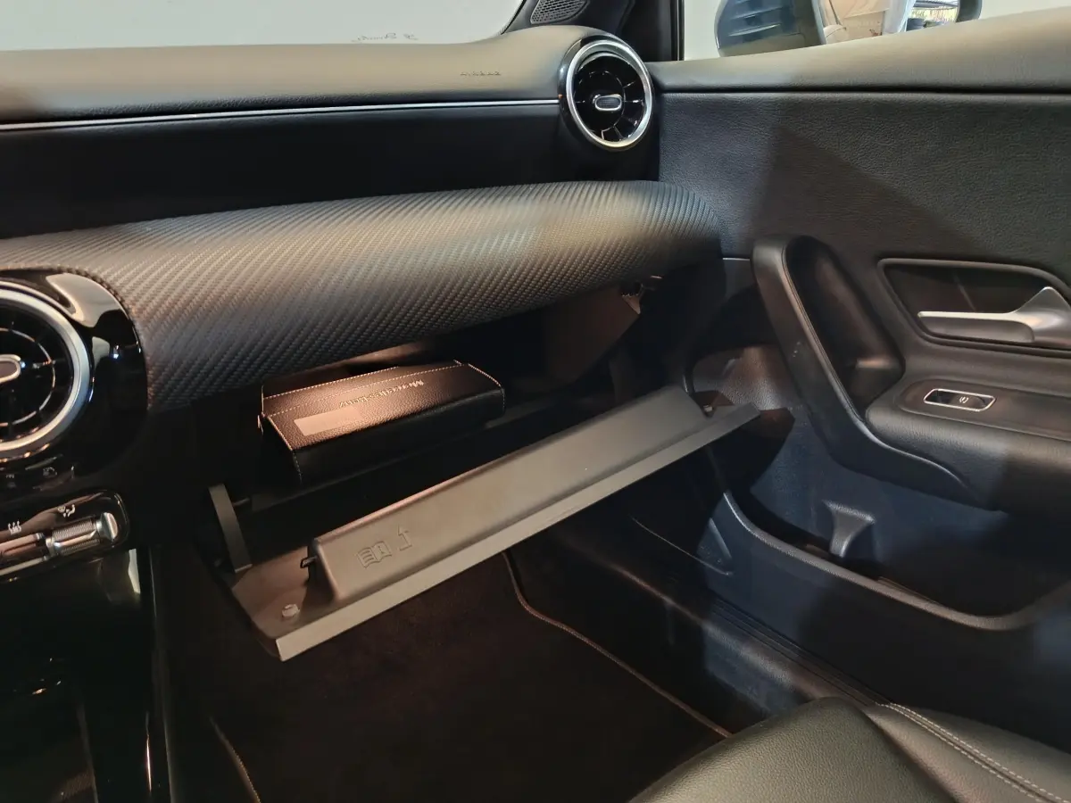 Intérieur côté passager de la Mercedes Classe A 250 e bleu, boîte à gants ouverte avec manuel visible, tableau de bord noir.