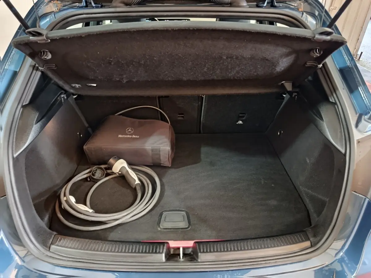 Coffre ouvert d'une Mercedes Classe A 250 e Business Line bleu, avec câble de recharge et sac de rangement Mercedes.