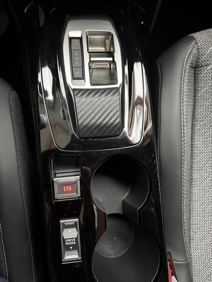 Vue rapprochée de la console centrale noire brillante du Peugeot 2008 Hybrid 145, avec sélecteur de vitesse et porte-gobelets.
