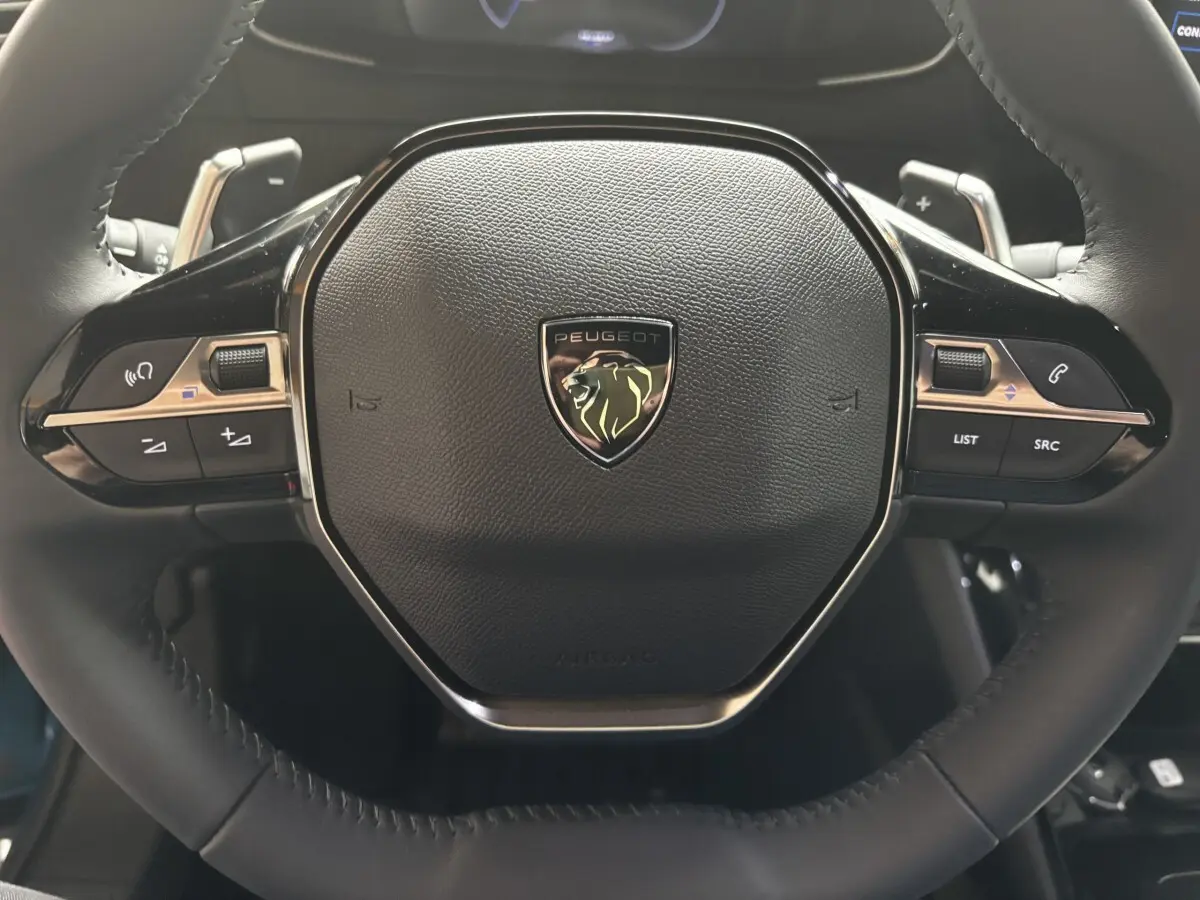 Gros plan sur le volant cuir noir du Peugeot 2008 Hybrid 145, avec commandes multifonctions et logo lion central.
