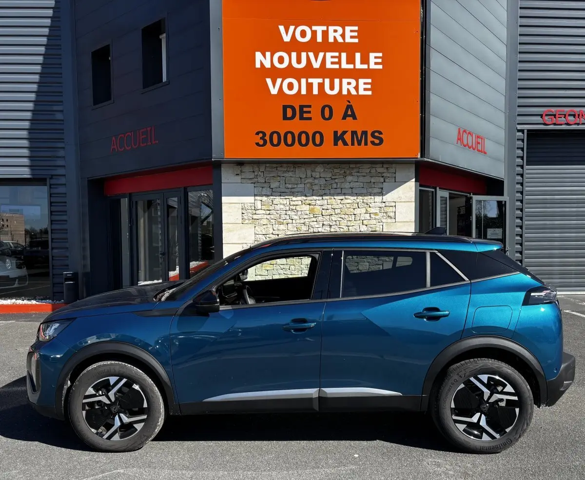 Profil latéral gauche d’un Peugeot 2008 bleu métallisé garé devant un bâtiment avec panneau orange.