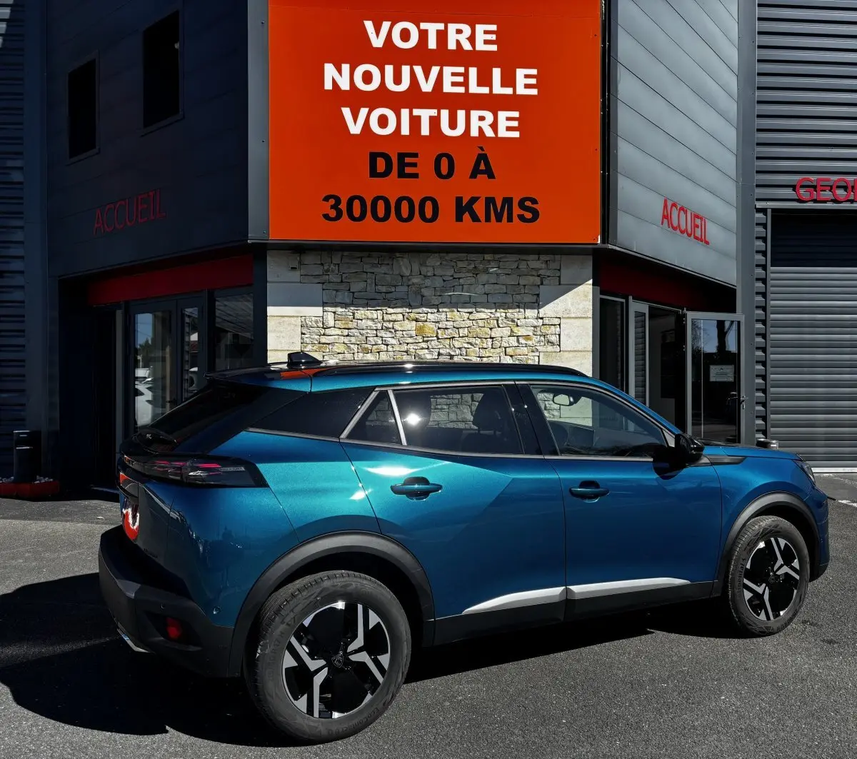 Vue côté droit arrière du Peugeot 2008 Hybrid 145 e-DCS6 Allure bleu métallisé garé devant un bâtiment commercial.