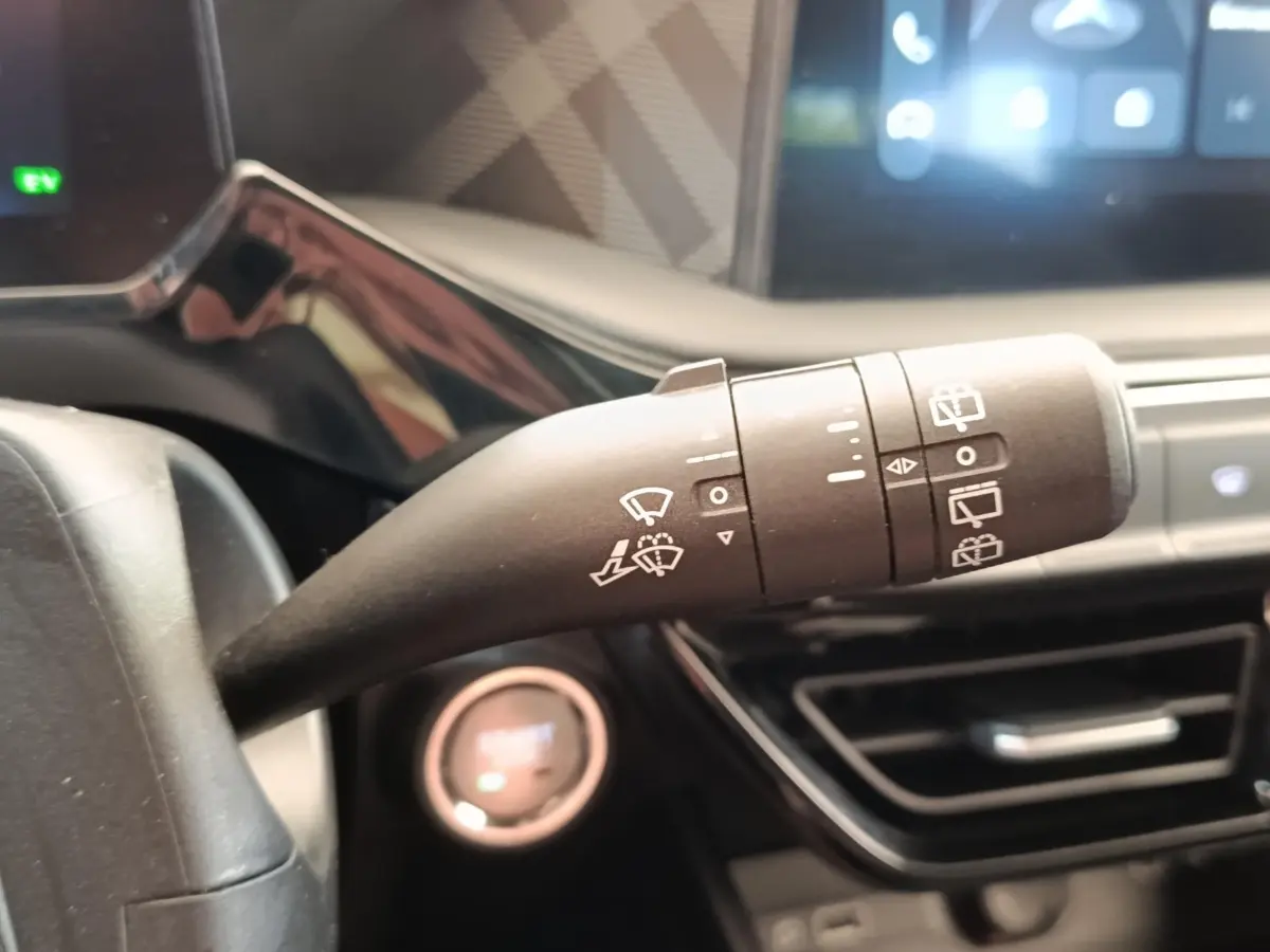 Gros plan sur la commande d’essuie-glace du volant d’une MG3 gris foncé, avec tableau de bord et écran tactile en arrière-plan.
