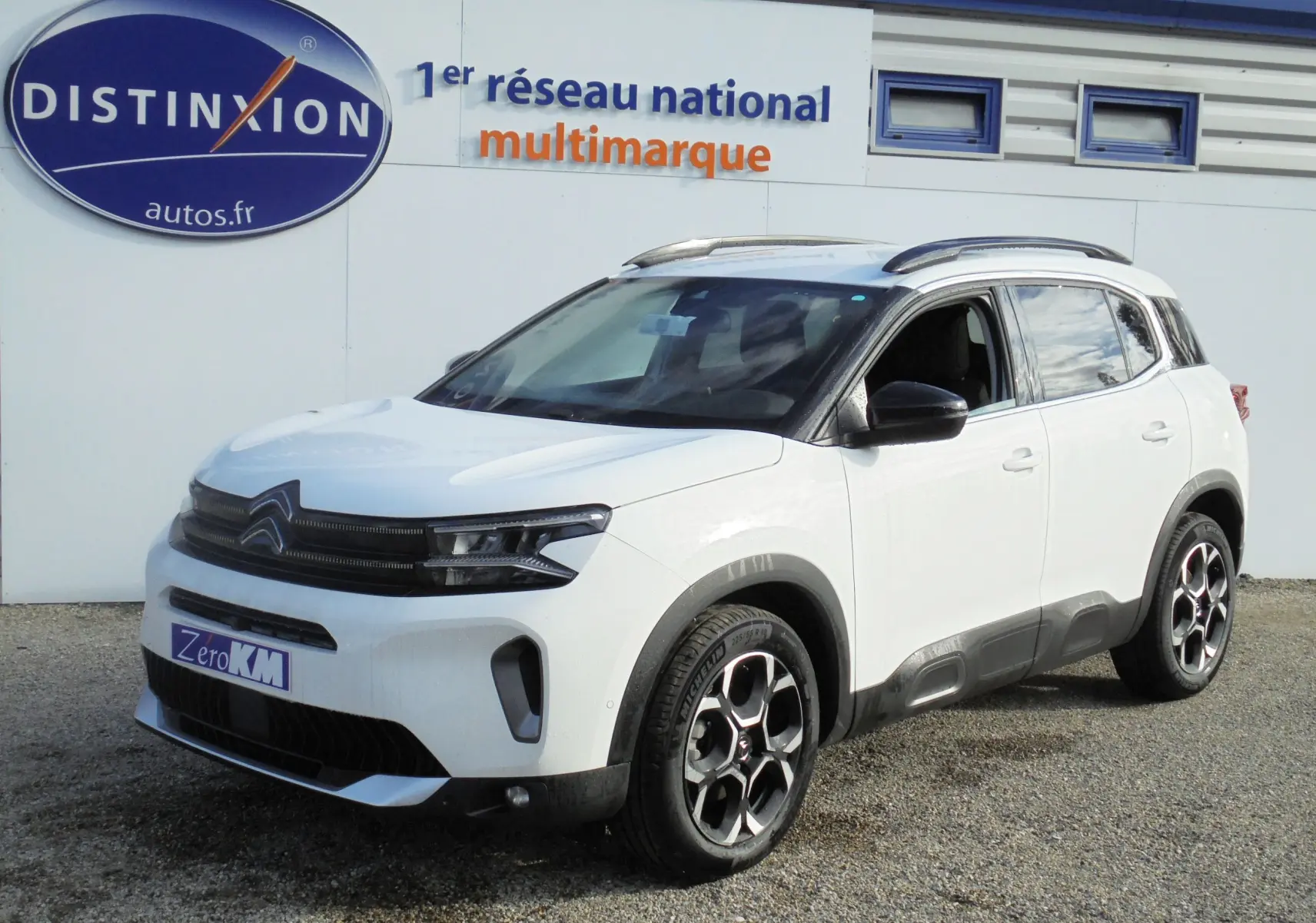 Citroën C5 Aircross blanc banquise en 3/4 avant droit avec jantes biton et barres de toit noires.