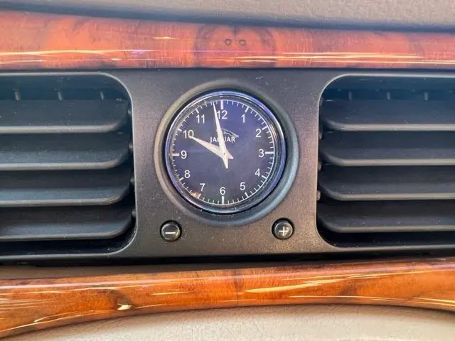 Gros plan sur l'horloge analogique Jaguar intégrée au tableau de bord en bois verni d'une Sovereign 3.2 V8 verte de 2002.