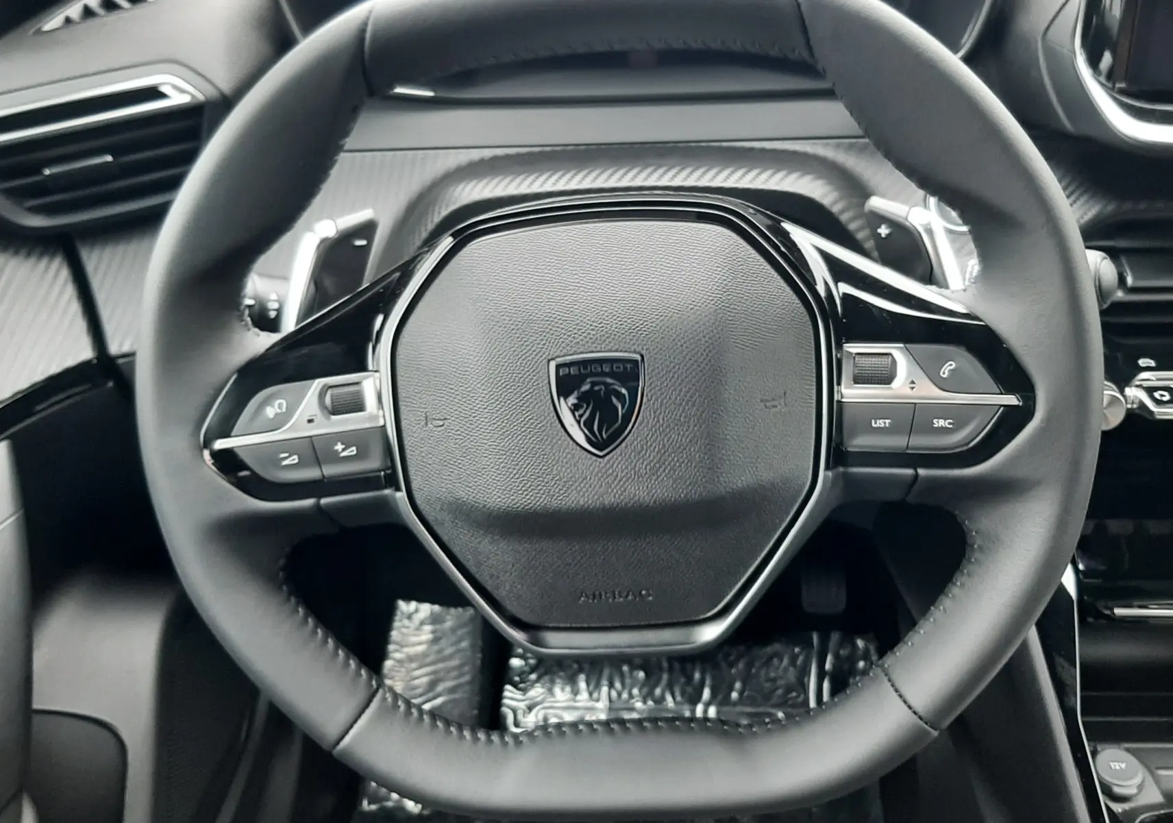 Vue rapprochée du volant cuir noir du Peugeot 2008 2025, avec commandes intégrées et tableau de bord numérique.