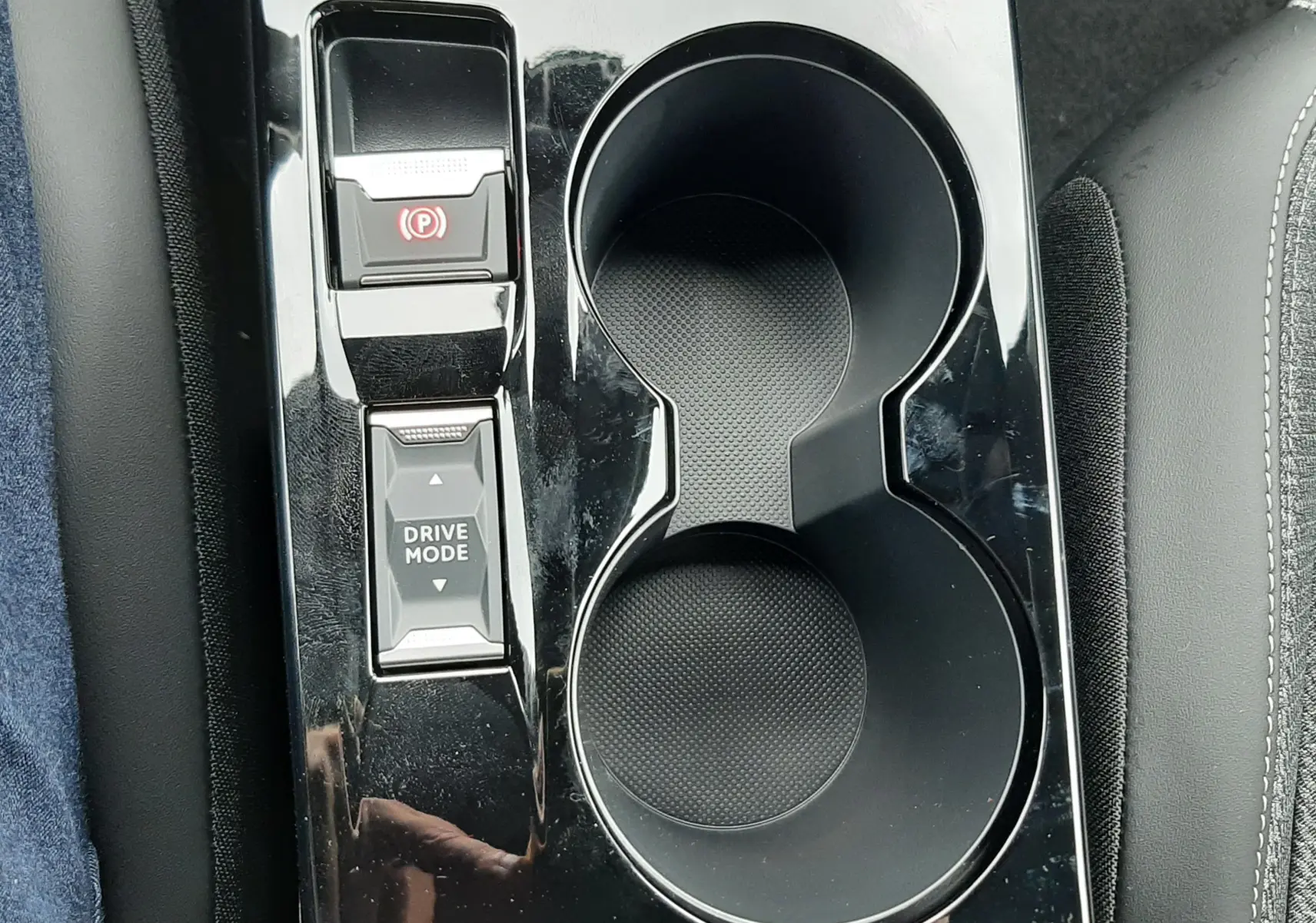Gros plan sur la console centrale noire brillante du Peugeot 2008 avec porte-gobelets et commandes Drive Mode et frein à main électronique.