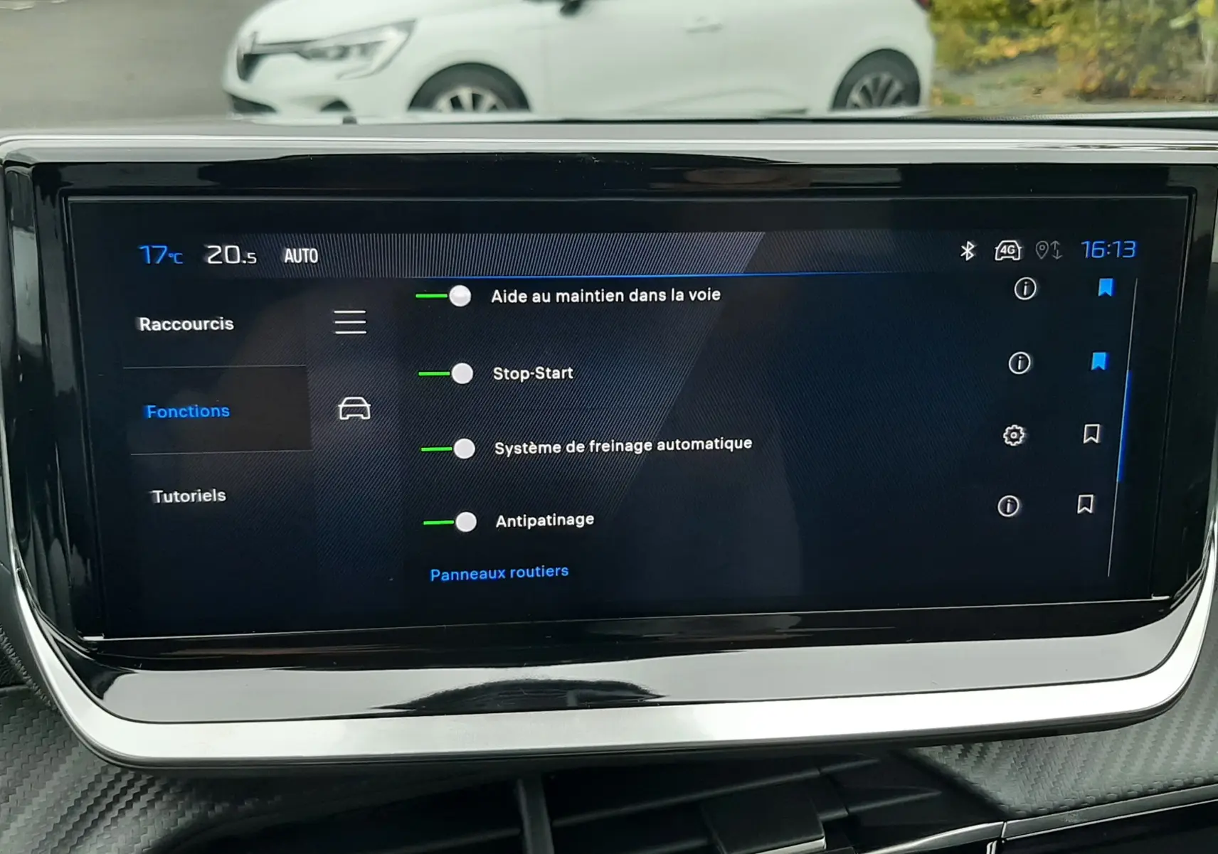 Écran tactile du système de navigation du Peugeot 2008 gris Artense, vue intérieure frontale avec voiture blanche en arrière-plan.