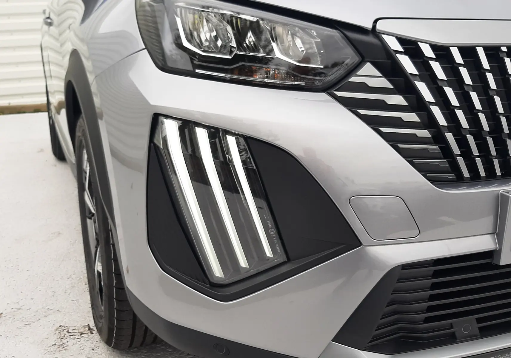 Gros plan sur l'avant droit du Peugeot 2008 gris Artense, mettant en valeur ses phares LED et la calandre distinctive.