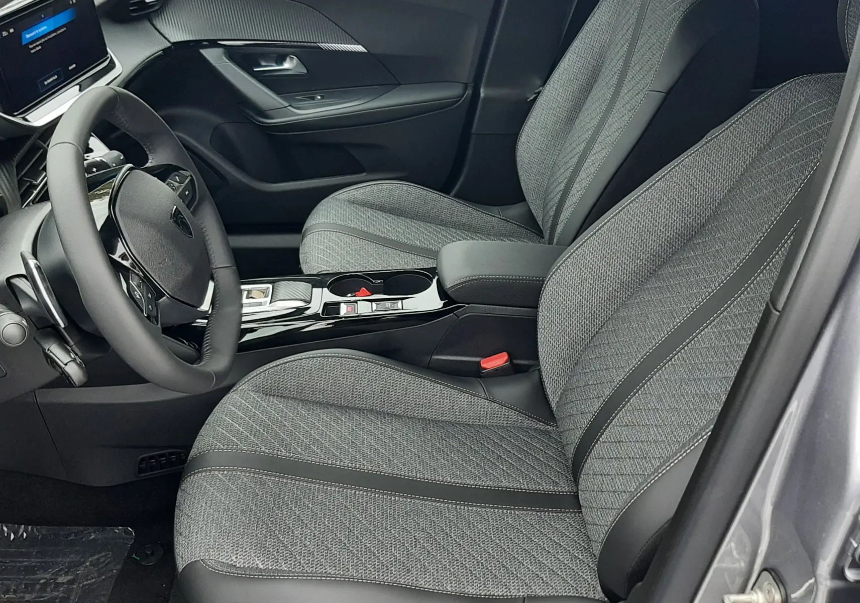 Intérieur côté conducteur du Peugeot 2008 gris Artense 2025, sièges tissu gris et tableau de bord moderne avec écran tactile.