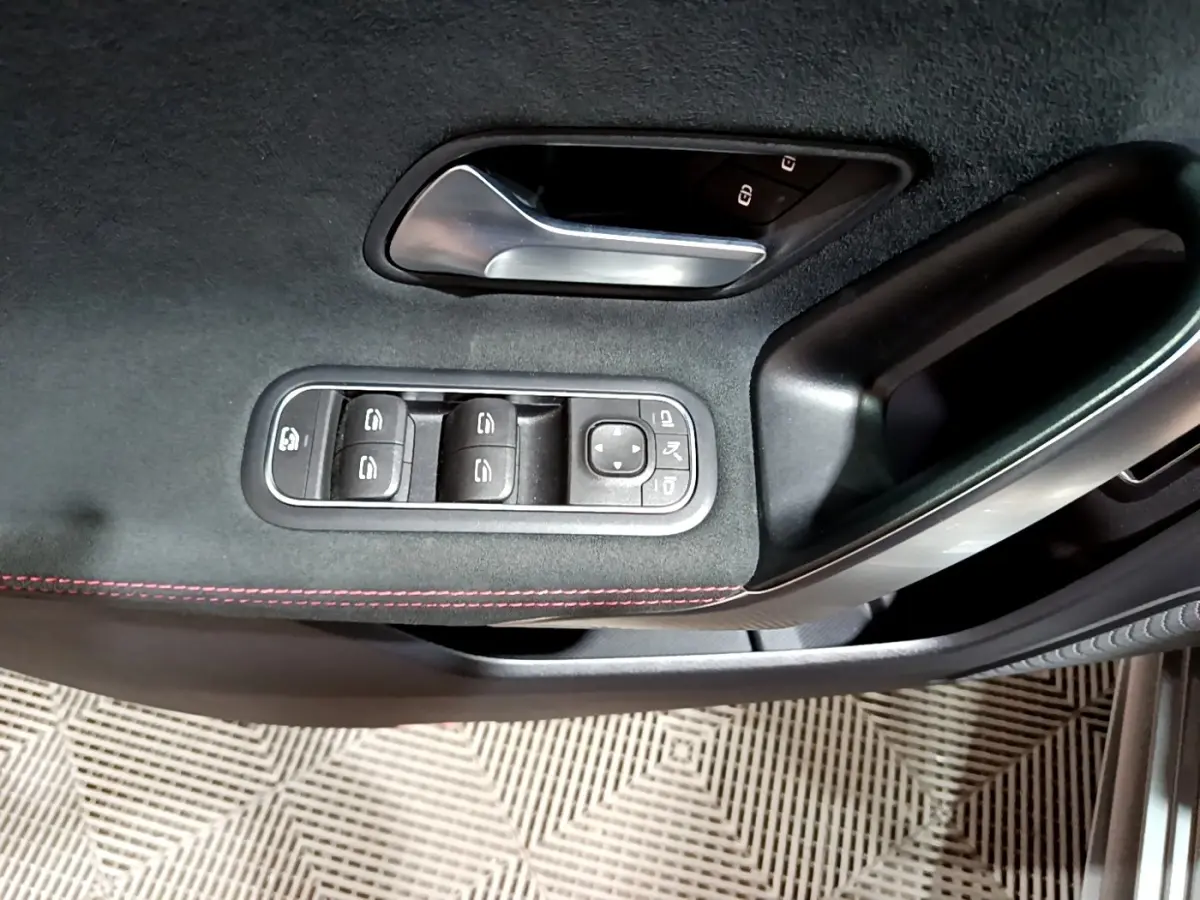 Gros plan sur la commande des vitres et poignée intérieure côté gauche d’une Mercedes Classe A gris foncé AMG Line.