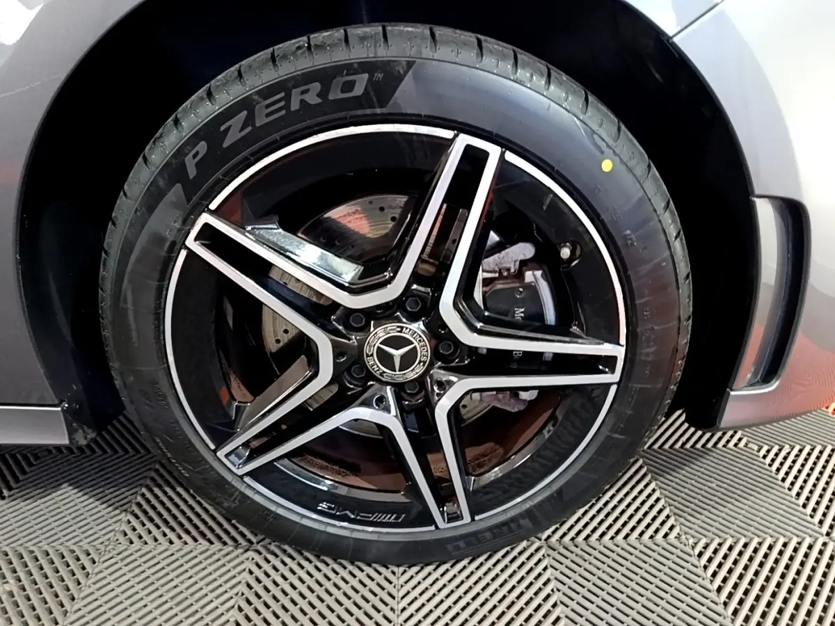 Gros plan sur la jante AMG noire et argentée avec logo Mercedes, montée sur pneu Pirelli P Zero, carrosserie gris foncé visible.