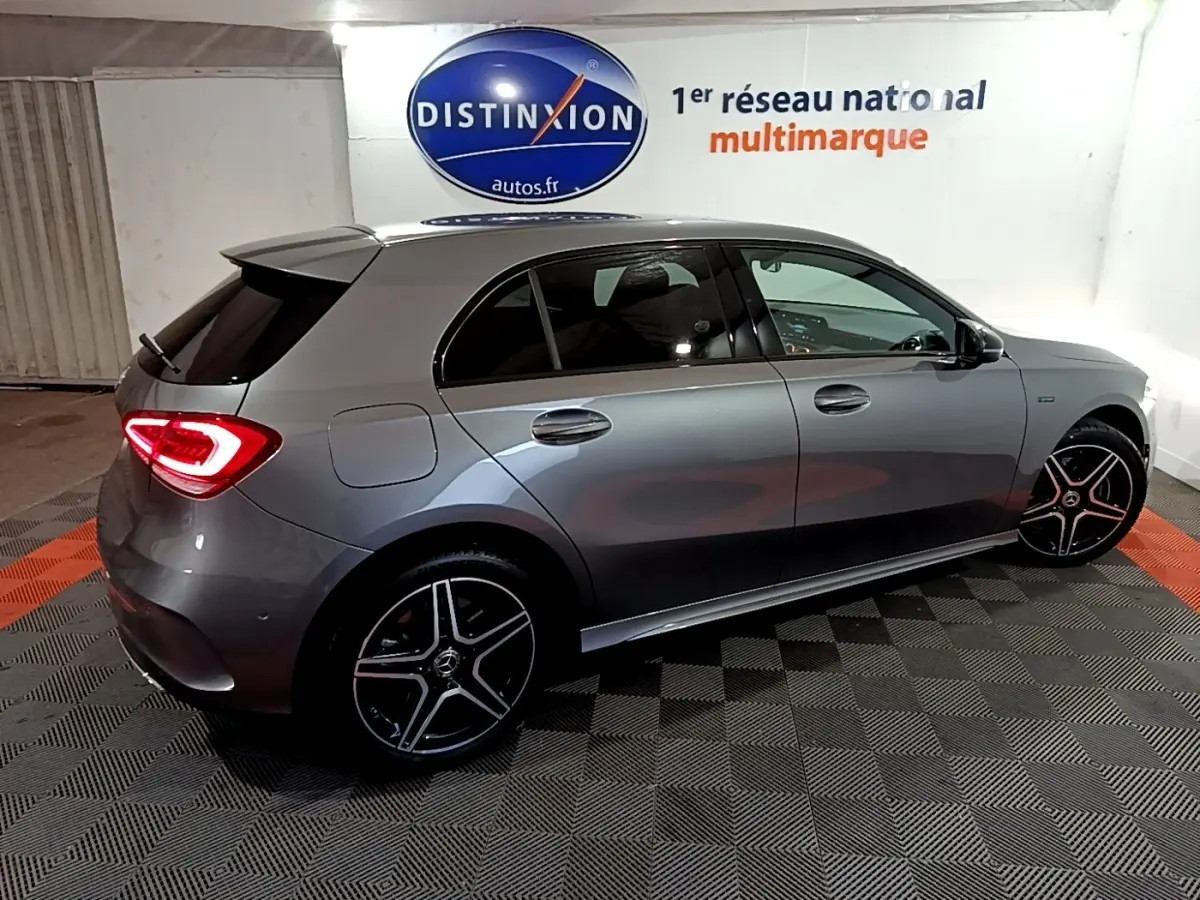 Vue latérale droite d'une Mercedes Classe A 250 e AMG Line gris foncé avec feux arrière LED allumés en intérieur showroom.