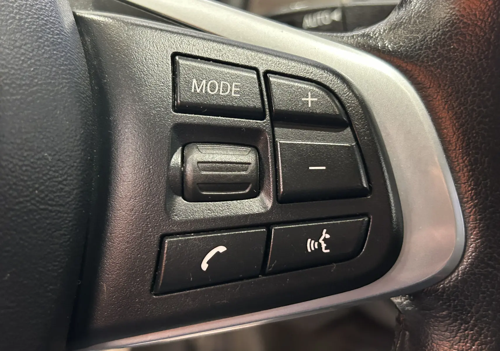 Gros plan sur les boutons de commande au volant côté gauche du BMW X1 blanc, avec touches mode, volume et téléphone.