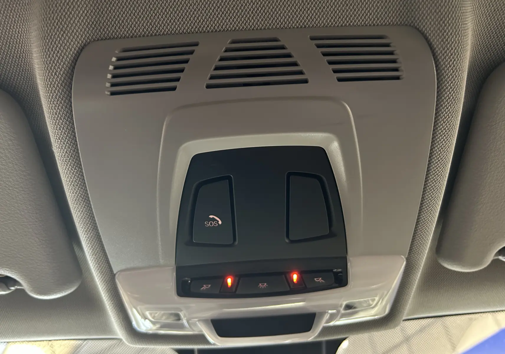 Vue en gros plan du plafonnier intérieur gris avec boutons SOS et éclairage activé dans un BMW X1 blanc 2018.