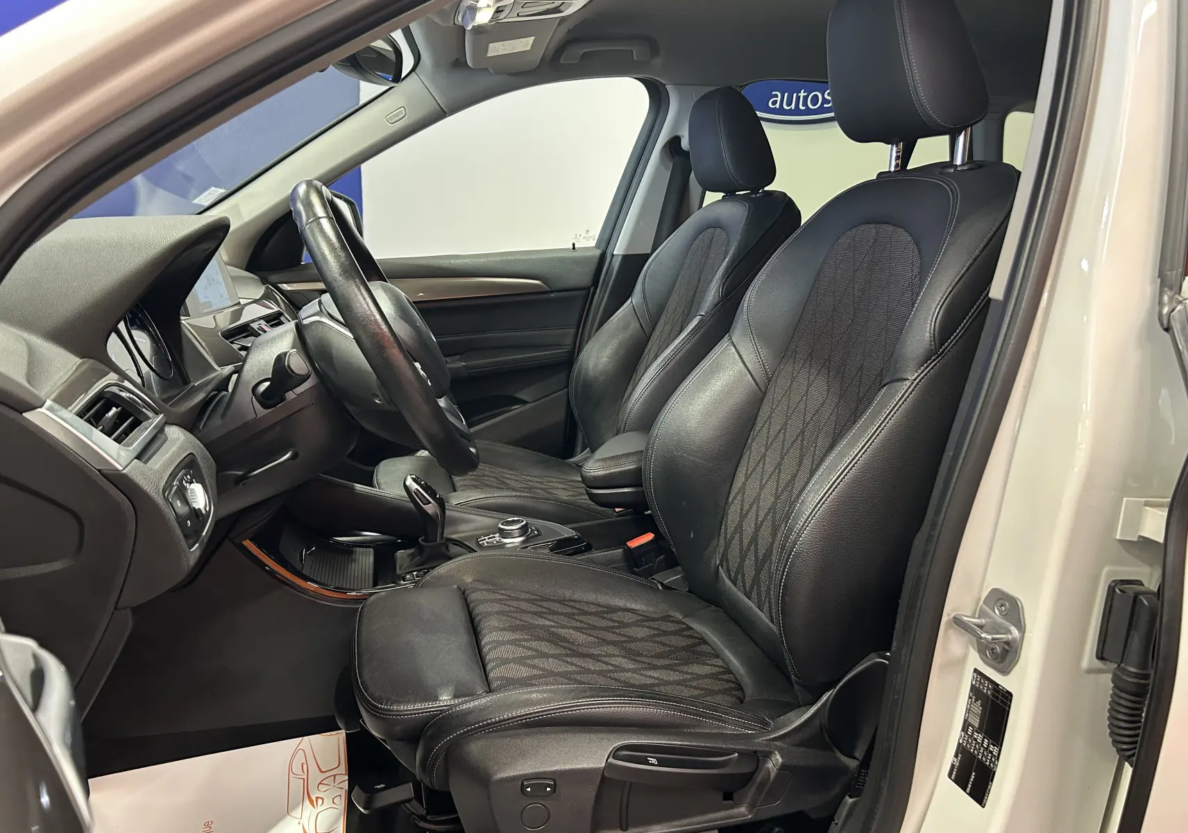 Vue intérieure côté conducteur d'un BMW X1 blanc 2018, sièges avant en cuir noir avec surpiqûres contrastantes.