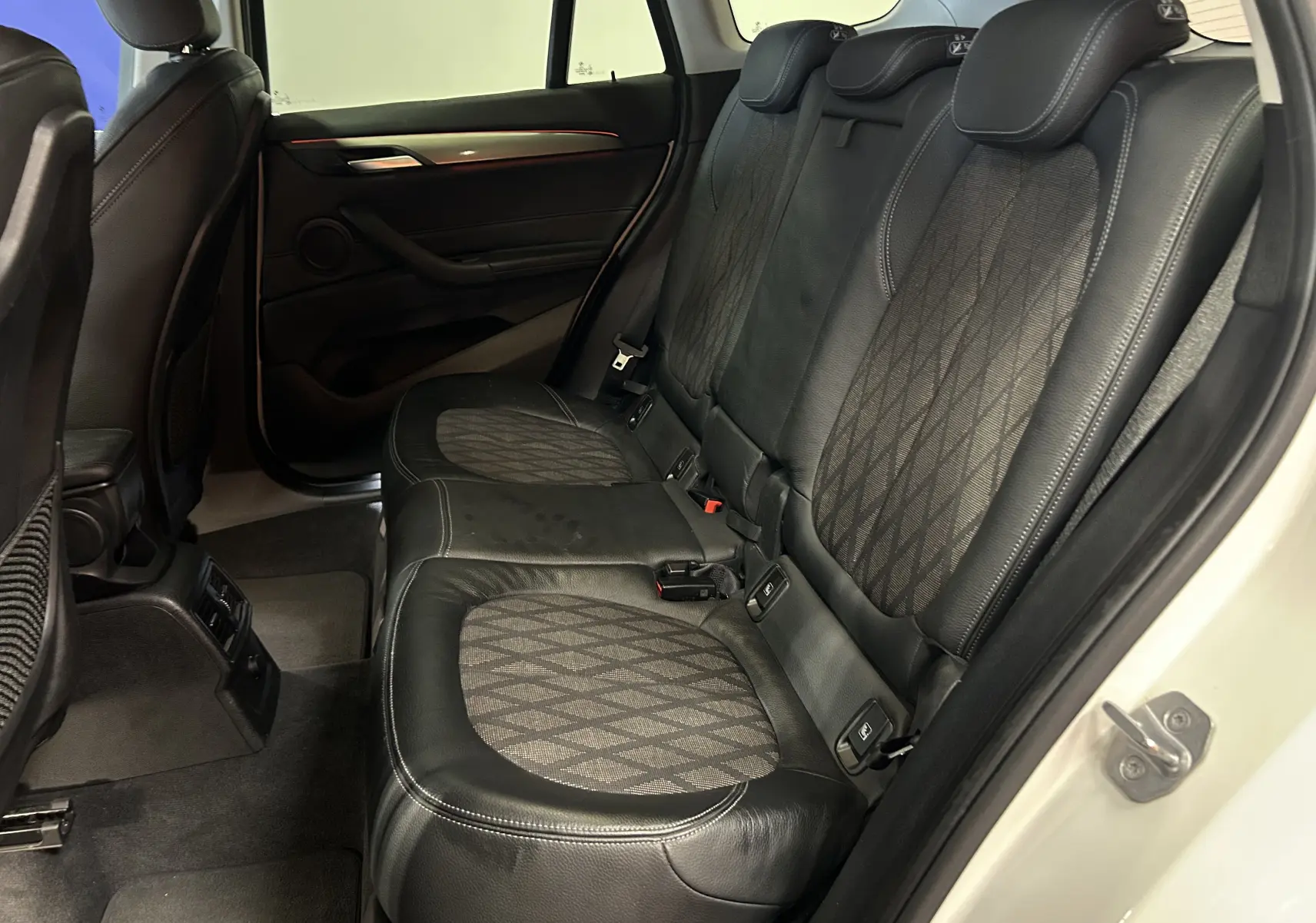 Vue intérieure côté droit des sièges arrière en cuir noir et tissu à motifs d'un BMW X1 blanc de 2018 avec porte ouverte.
