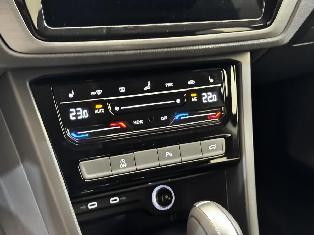 Vue rapprochée du tableau de bord noir du Volkswagen Touran 2024, montrant la climatisation digitale et la console centrale.