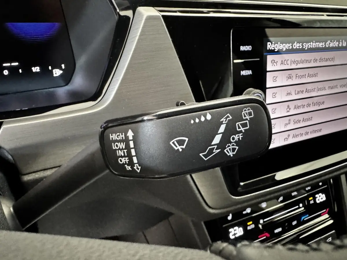 Gros plan sur la commande des essuie-glaces dans l’habitacle du Volkswagen Touran 2024, écran tactile en arrière-plan.