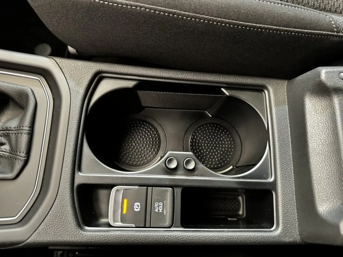 Gros plan sur la console centrale noire du Volkswagen Touran 2024 avec porte-gobelets et frein à main électrique allumé.
