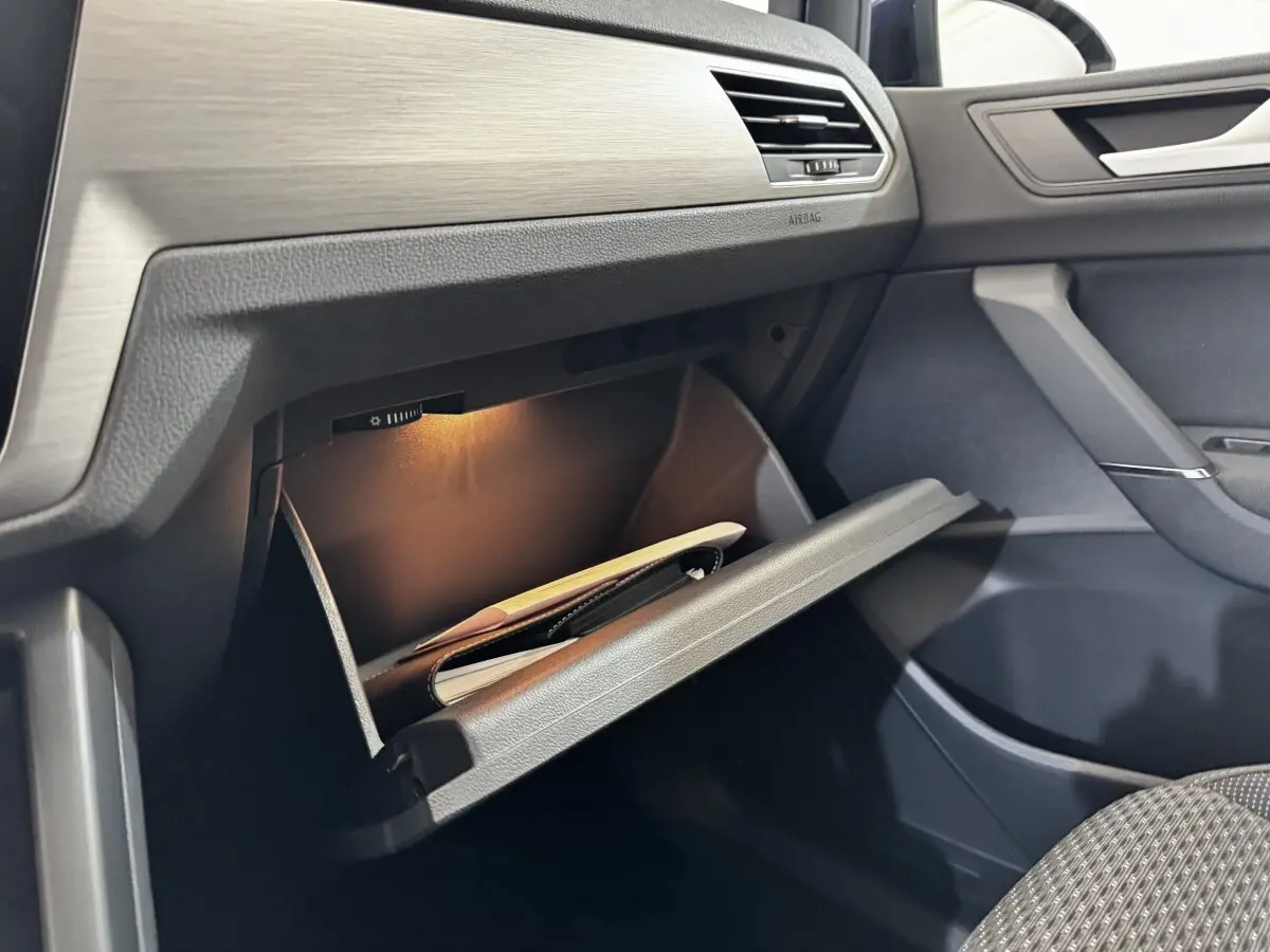 Gros plan sur la boîte à gants ouverte côté passager du Volkswagen Touran 2024 avec éclairage intérieur et tableau de bord gris.