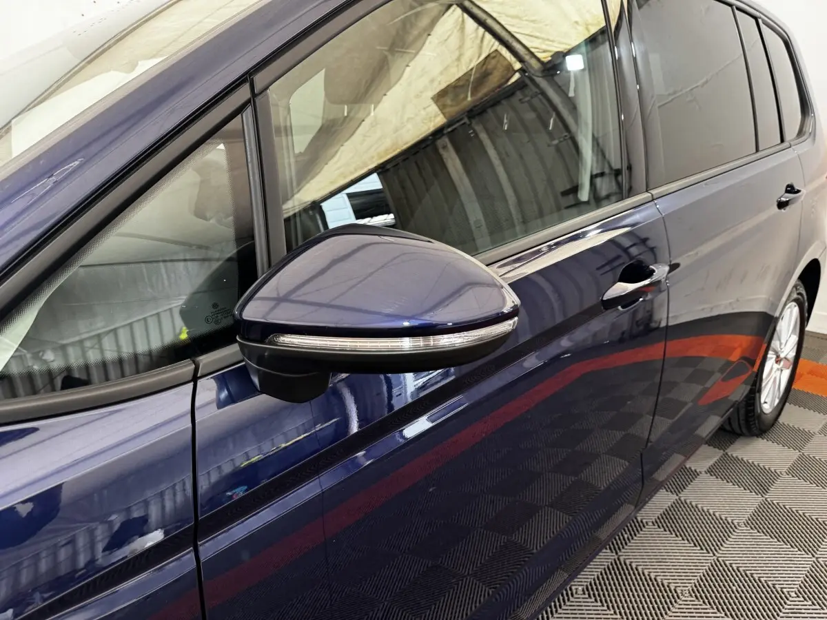 Vue rapprochée côté gauche du Volkswagen Touran bleu 2024, mettant en valeur la portière et le rétroviseur avec clignotant intégré.