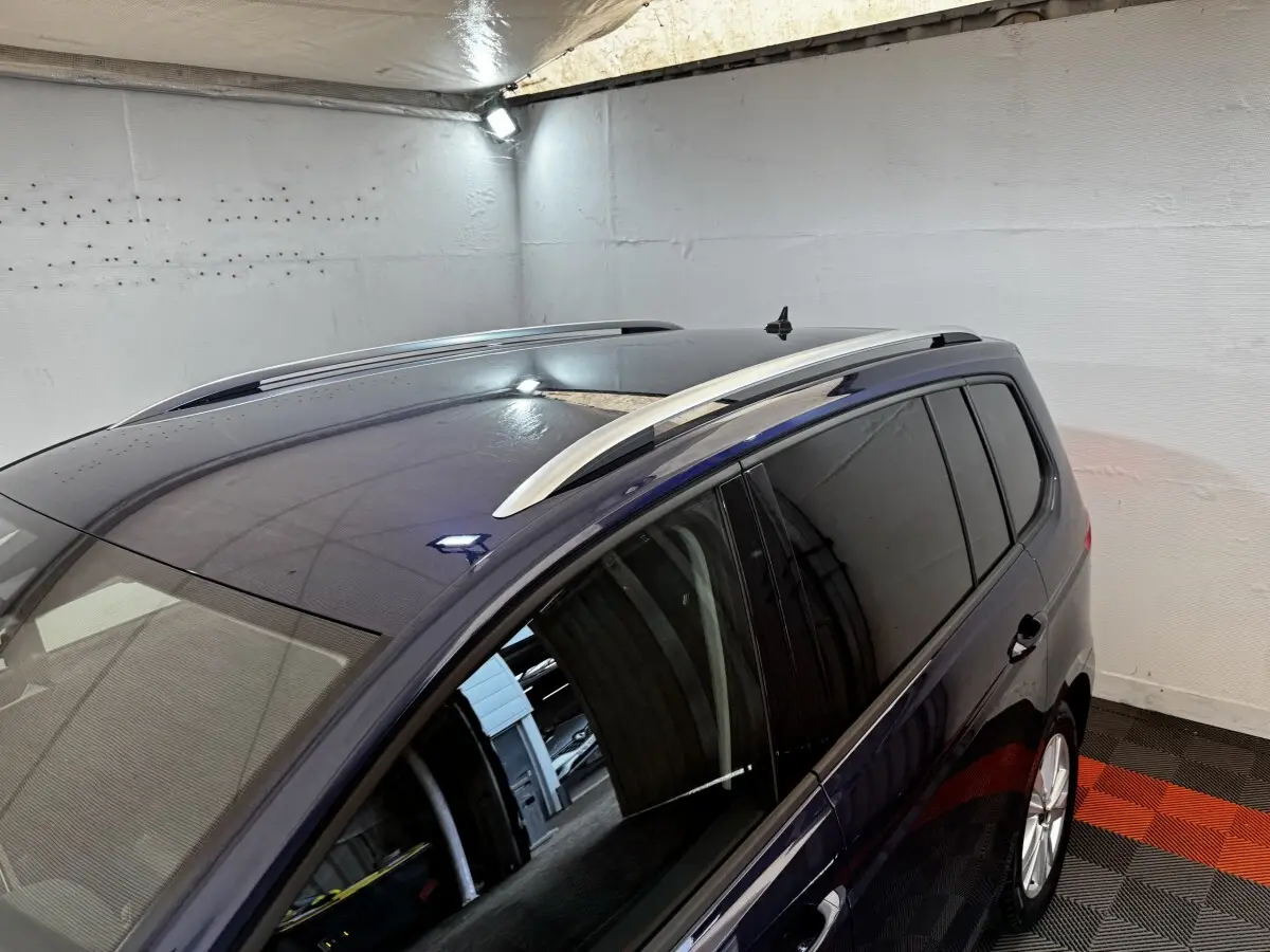 Vue en plongée côté droit du Volkswagen Touran bleu 2024 avec barres de toit argentées et toit panoramique.