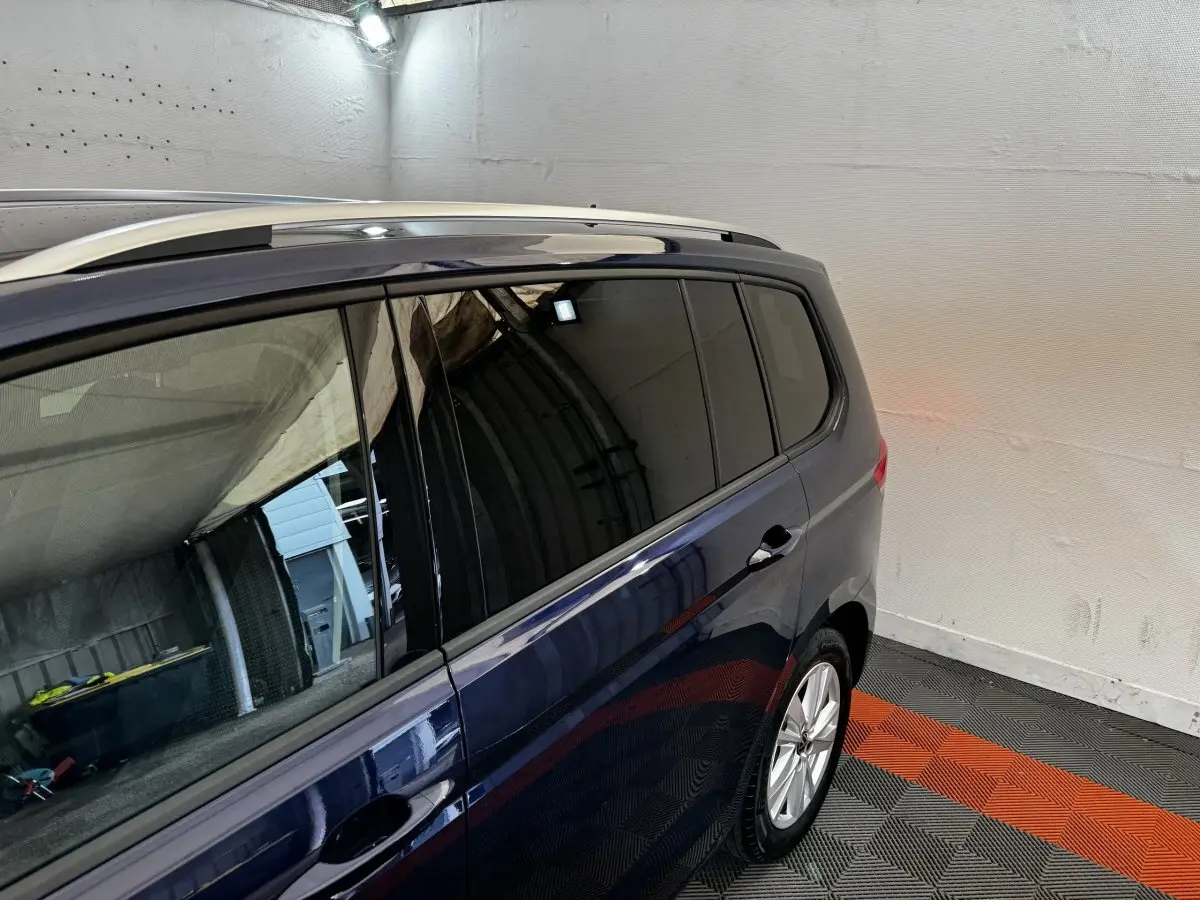 Vue latérale droite du Volkswagen Touran bleu 2024, avec vitres teintées et barres de toit chromées visibles.