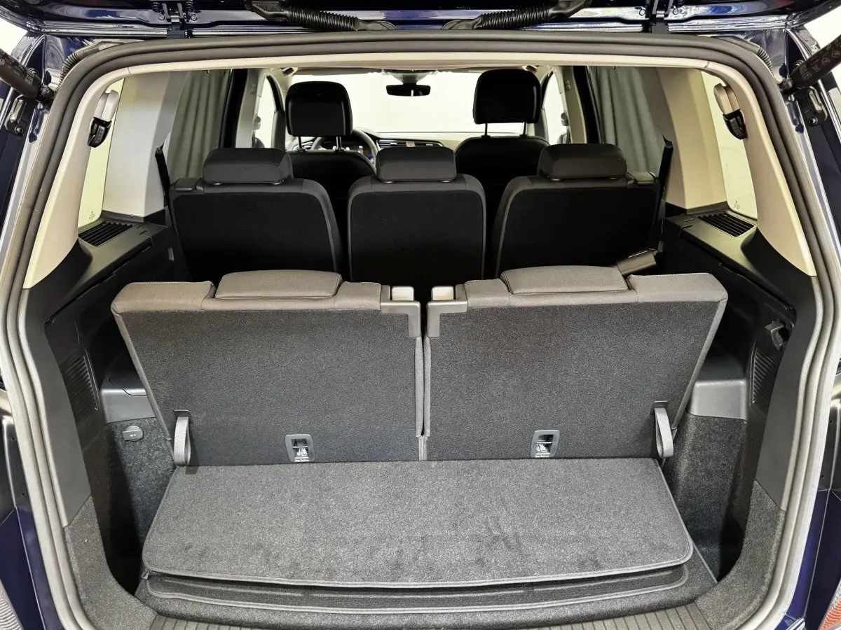 Vue arrière du coffre ouvert du Volkswagen Touran bleu 2024, montrant la troisième rangée de sièges rabattables.