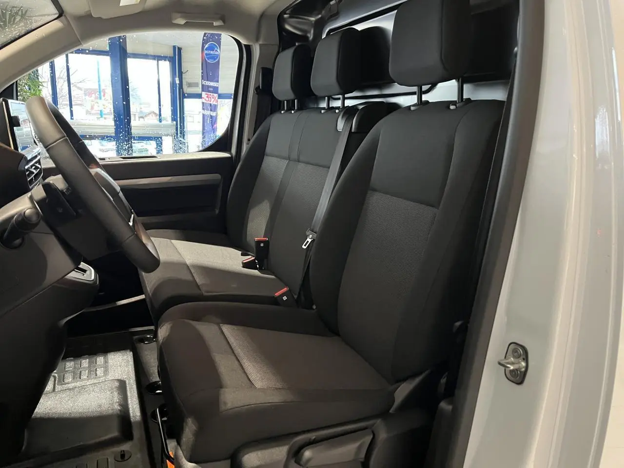 Intérieur du Peugeot Expert Fourgon blanc 2024 vu côté gauche, sièges tissu bi-ton noir-gris avec volant cuir.