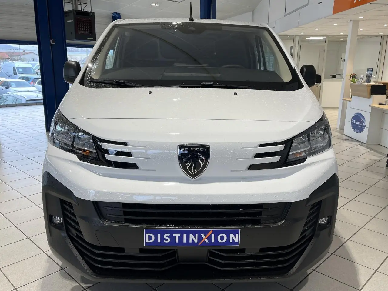Vue frontale d'un Peugeot Expert Fourgon blanc 2024 avec logo lion et calandre noire en showroom.