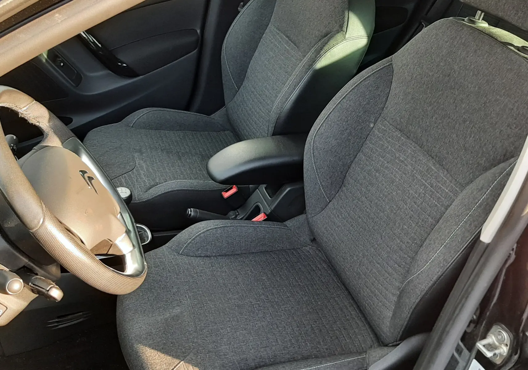 Vue intérieure côté conducteur de la Citroën C3 noire, sièges en tissu gris et volant avec commandes intégrées.