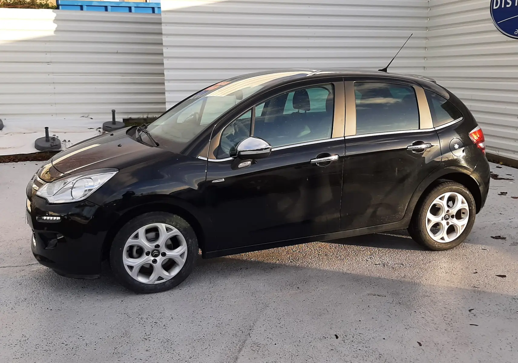 Citroën C3 noire vue de profil côté gauche, avec jantes alliage et rétroviseurs chromés sur fond urbain.