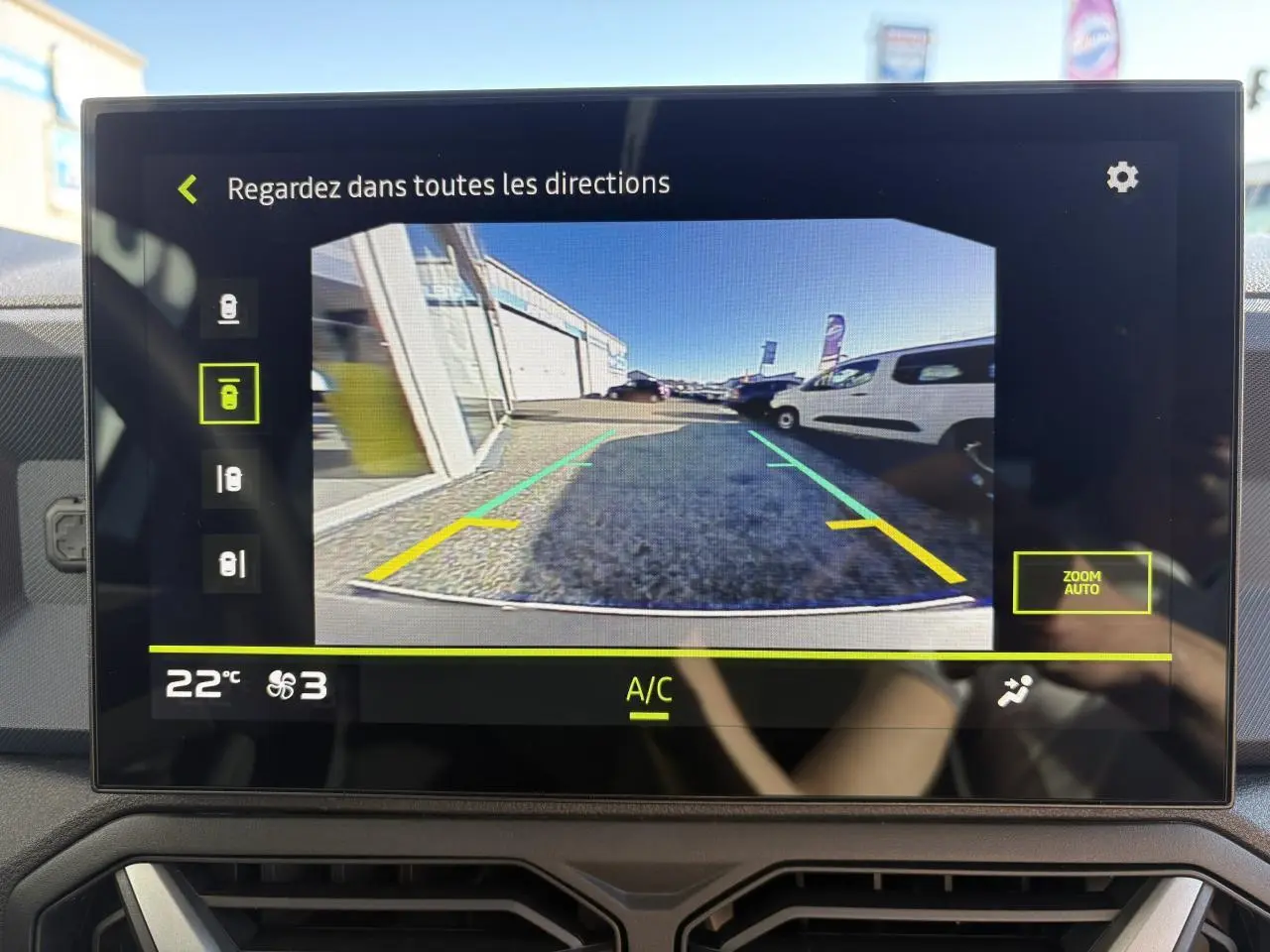 Écran tactile montrant la caméra de recul du Dacia Duster blanc métallisé, vue arrière avec lignes de guidage colorées.