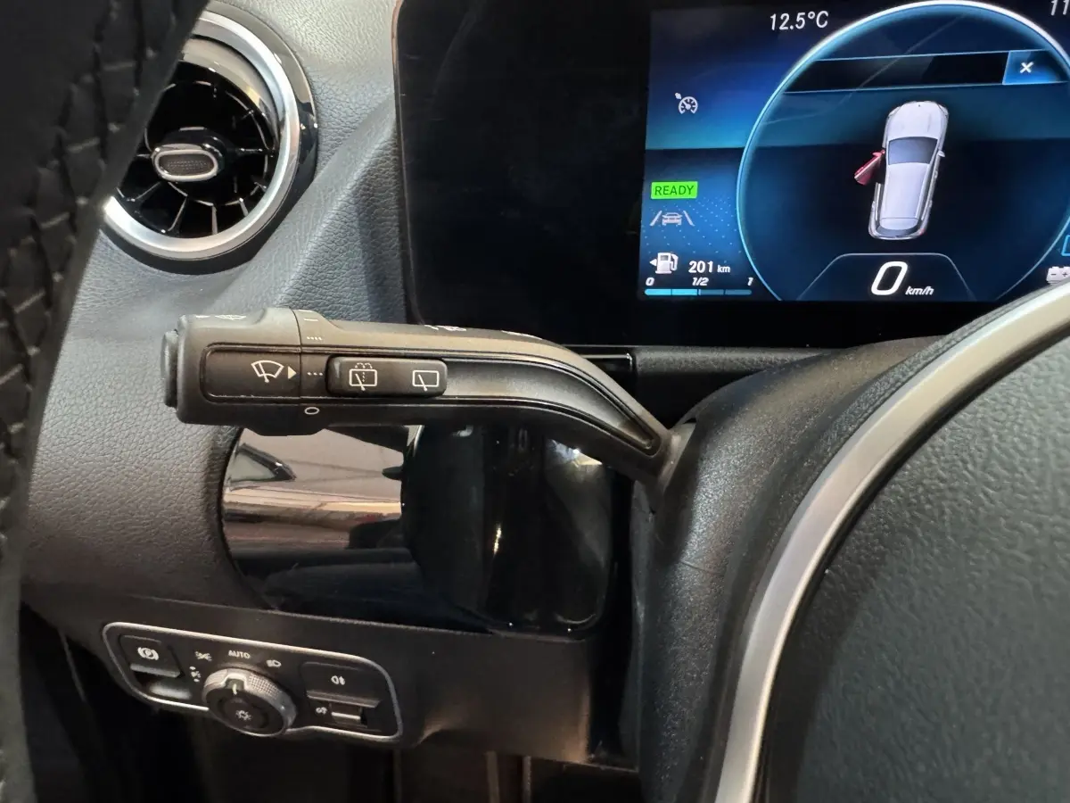Gros plan sur la commande d’essuie-glace à gauche du volant cuir noir dans le tableau de bord numérique d’une Mercedes GLA 250 e gris foncé.