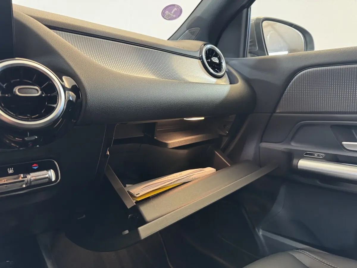 Intérieur côté passager du Mercedes GLA 250 e gris foncé 2023 avec boîte à gants ouverte et aérateurs ronds noirs.