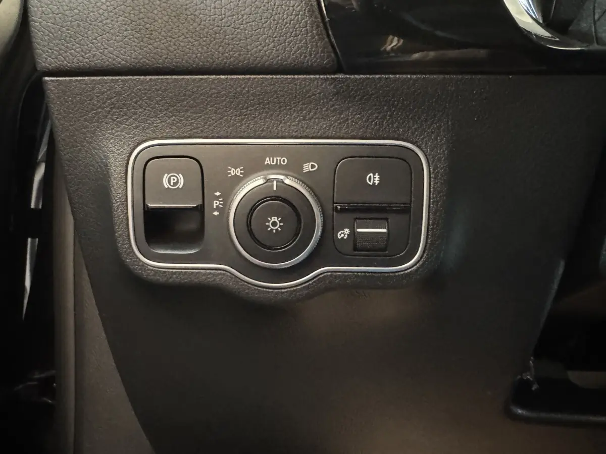 Gros plan sur les commandes d’éclairage et frein à main électrique du tableau de bord noir du Mercedes GLA 250 e 2023.