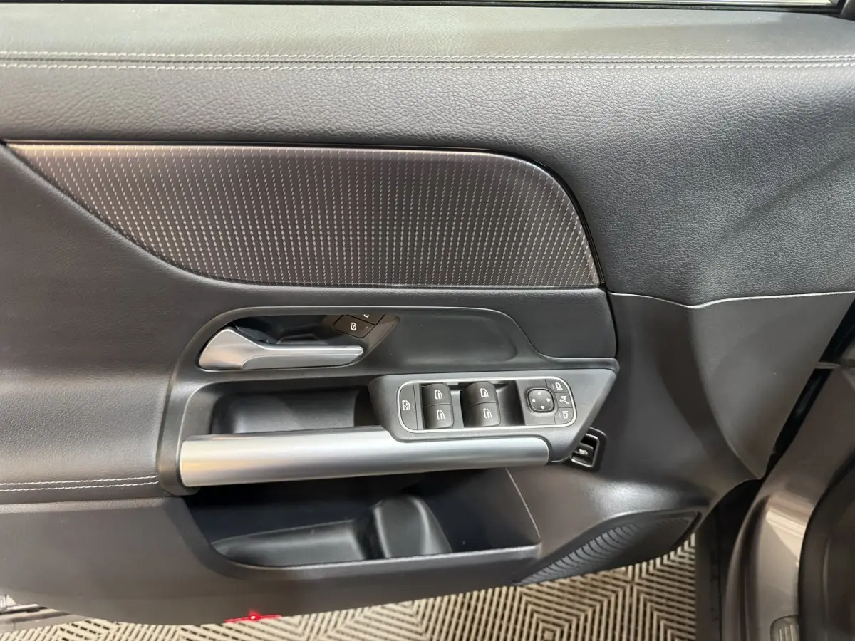 Vue intérieure de la porte avant gauche d'une Mercedes GLA 250 e Business Line gris foncé, avec commandes électriques et poignée argentée.