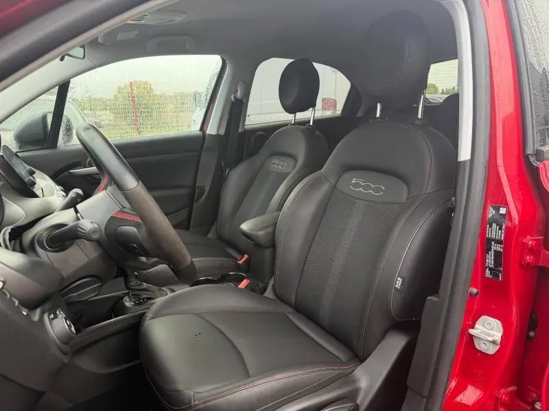 Vue intérieure côté conducteur du FIAT 500X rouge Passione pastel, sièges en cuir noir avec logo 500 brodé.