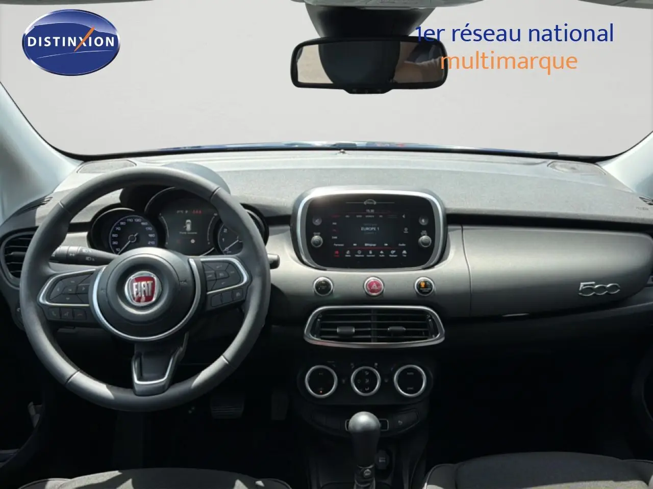 Vue intérieure frontale du tableau de bord et volant de la Fiat 500X 2024 en bleu Venezia, avec écran tactile central et commandes intégrées.