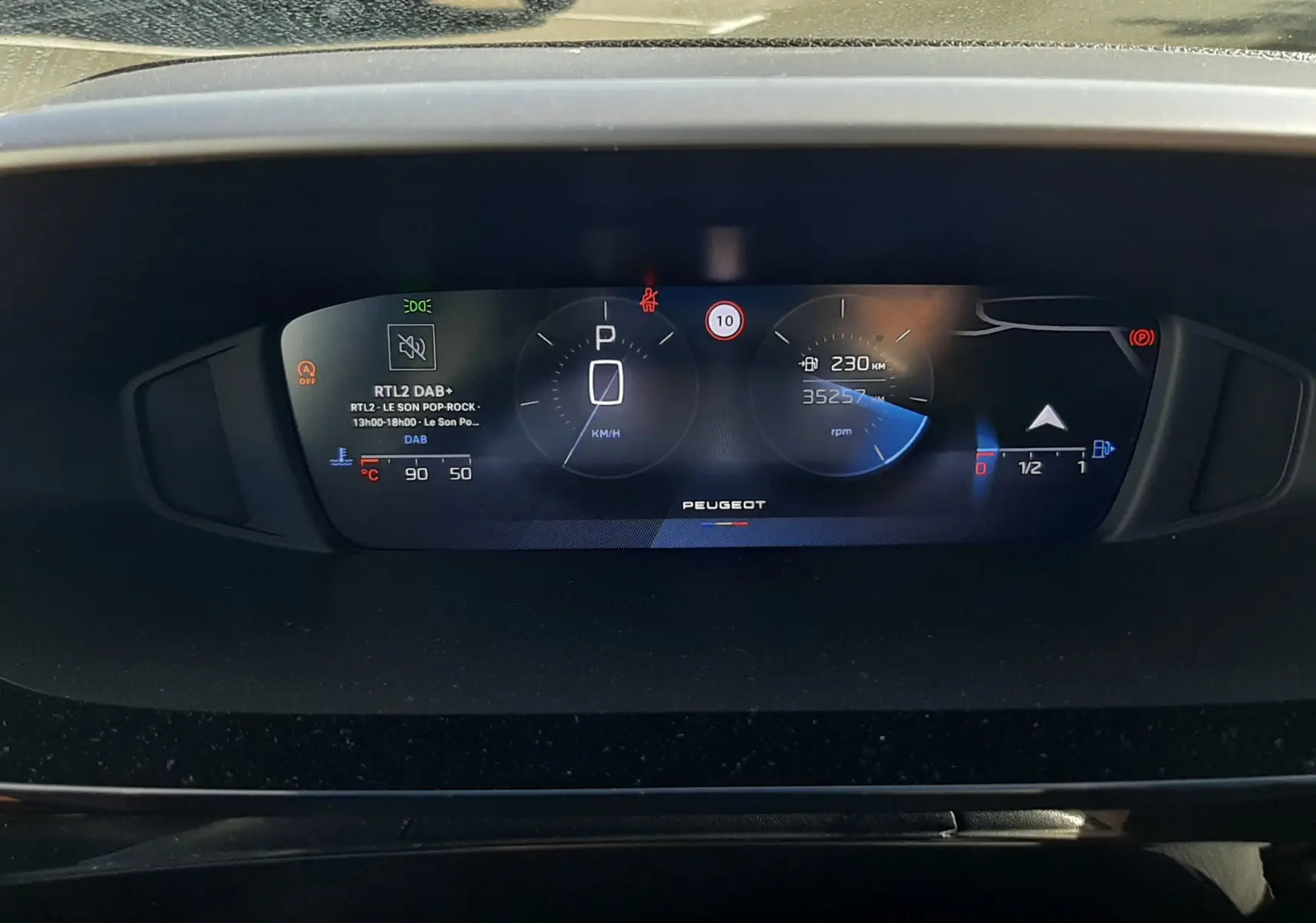 Tableau de bord numérique de Peugeot 308 blanc, affichant la vitesse à l'arrêt et le compteur kilométrique.