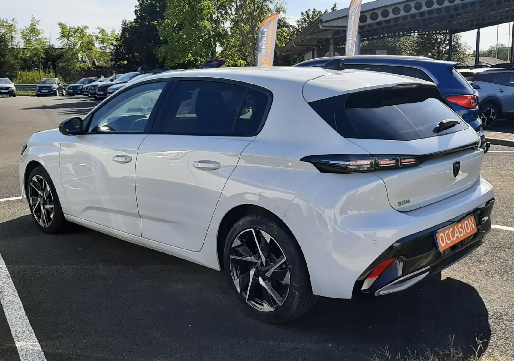 Peugeot 308 blanche vue 3/4 arrière droit, avec jantes noires et feux arrière LED distinctifs.