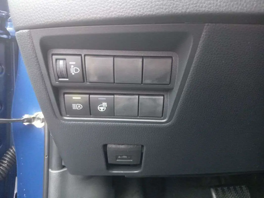 Panneau de commandes latéral gauche noir dans Toyota Yaris 1.5 Hybrid 116 BVA Design Plus 2025, avec réglage phares et fonction arrêt auto.