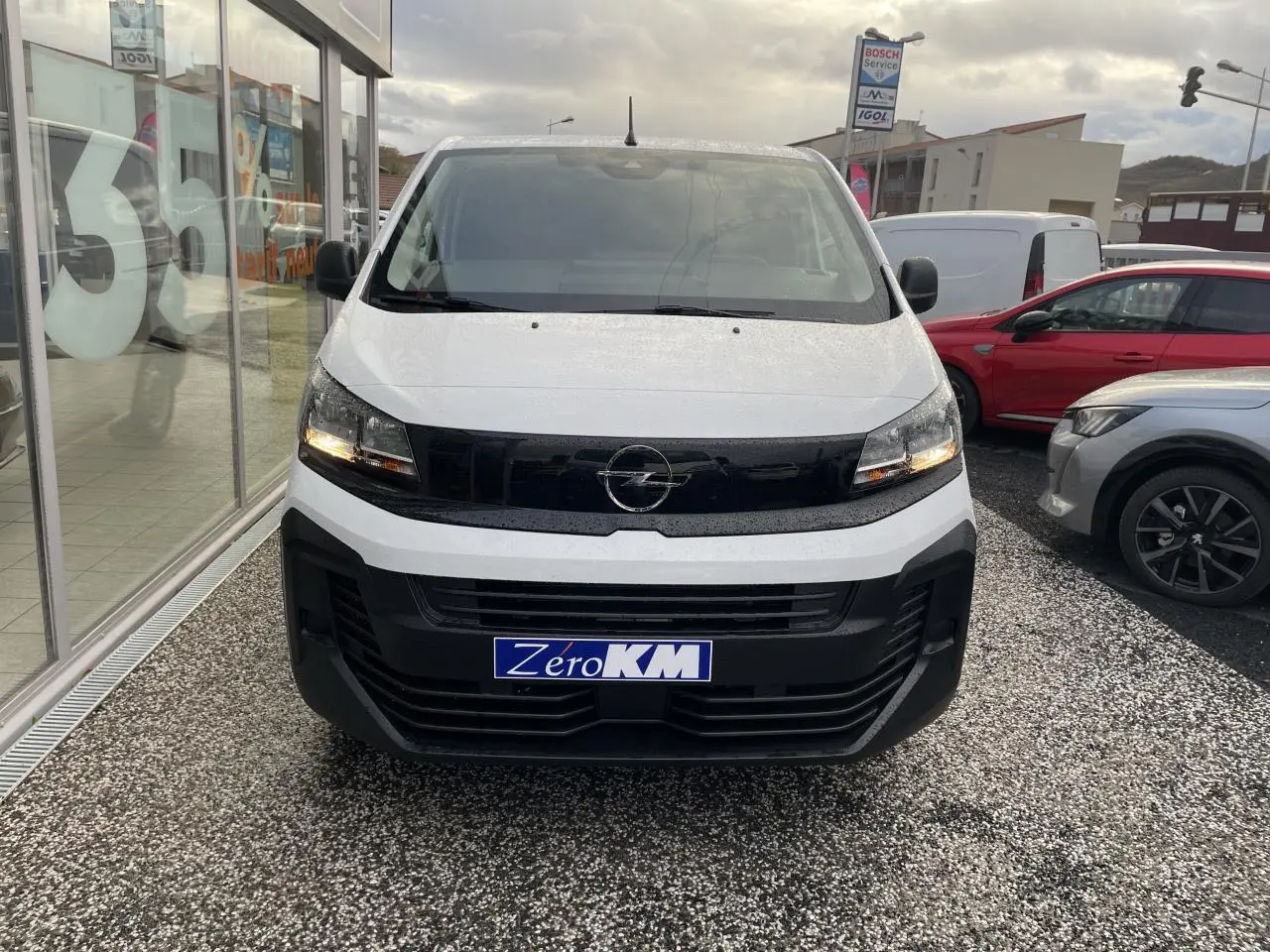 Vue de face d’un Opel Vivaro blanc 2024 avec calandre noire et feux allumés sur parking.